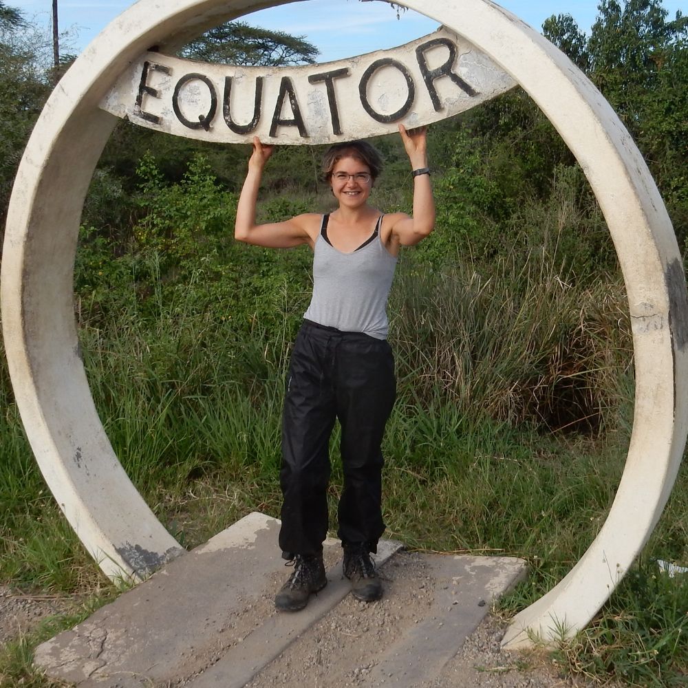 A photo of Imogen Cauthery, a brain injury survivor, standing and smiling at the equator point in Uganda.